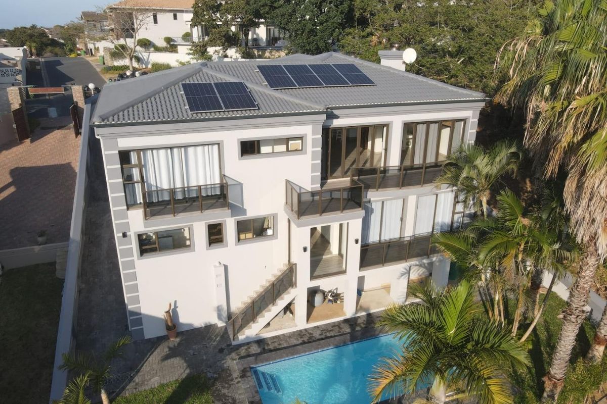 Aerial view of a modern multi-story house featuring a tiled roof with solar panels, multiple balconies, an external staircase, and a private swimming pool.