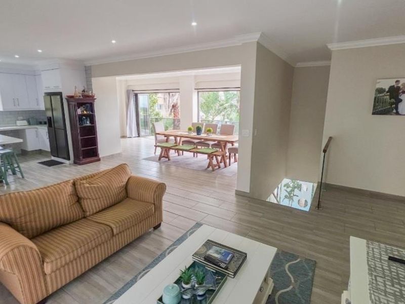 Spacious open-plan living area featuring a modern kitchen, dining space with sliding doors to a balcony, and a staircase with glass balustrade.