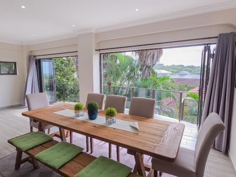 Spacious dining area featuring large bi-fold doors that open onto a balcony, providing ample natural light and views of the surrounding greenery.