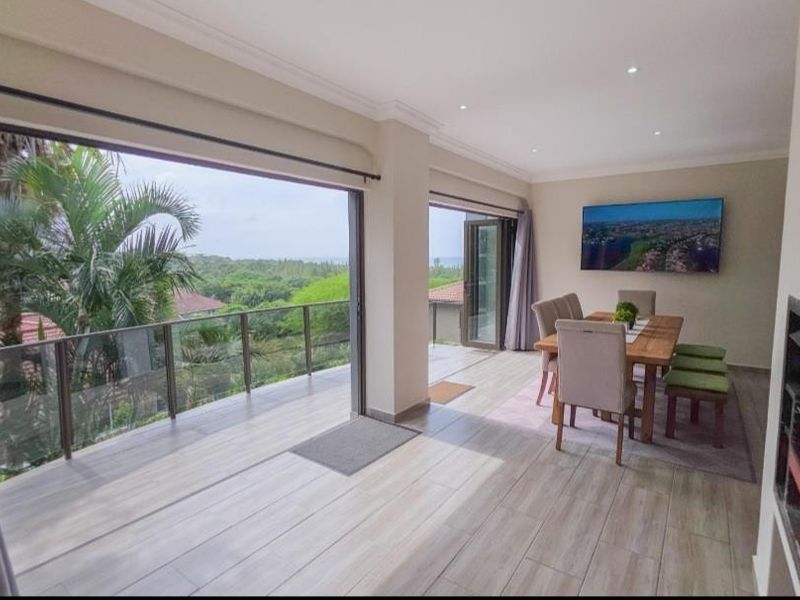 Spacious open-plan living and dining area featuring large stacking doors that open onto a balcony with scenic views and a built-in fireplace.