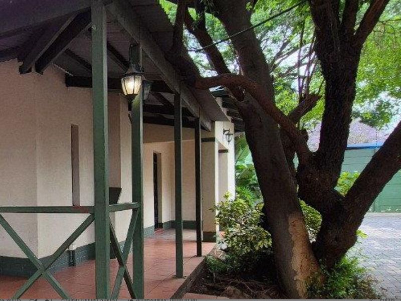 A covered outdoor patio area featuring tiled flooring, timber support posts, and railing, providing a shaded space adjacent to the garden.