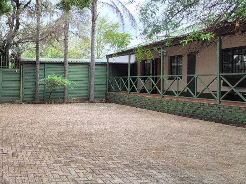 A paved driveway leading to a house with a covered veranda, featuring timber fencing and a brick retaining wall.