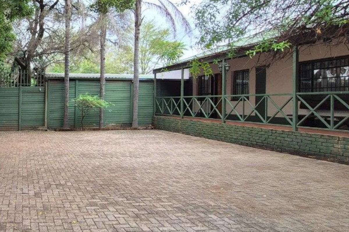 A paved driveway leading to a house with a covered veranda, featuring timber fencing and a brick retaining wall.