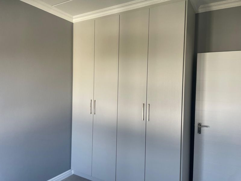 A clean, modern bedroom featuring neutral grey walls, white trim, and floor-to-ceiling built-in cupboards with contemporary handles.