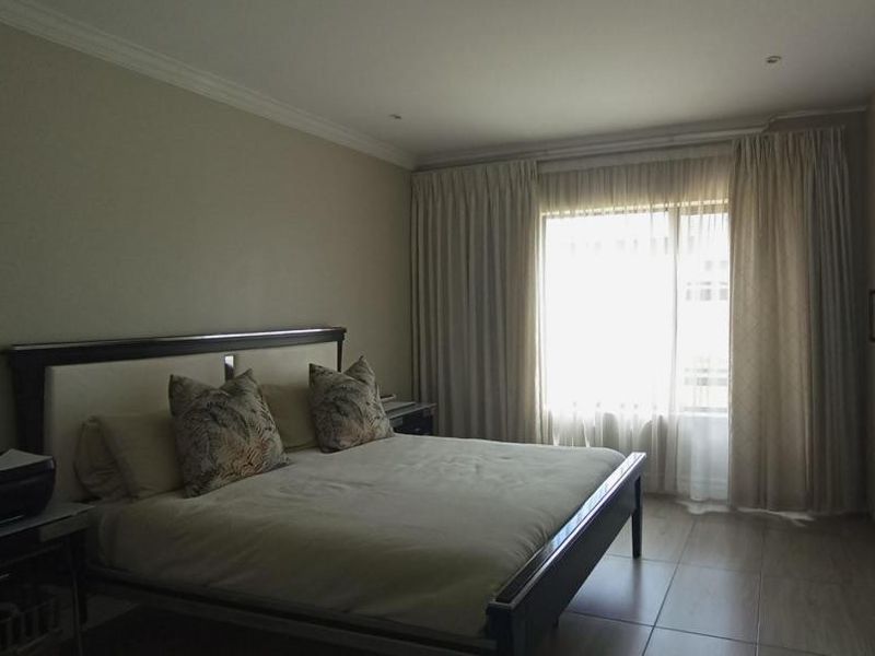 A well-maintained bedroom featuring tiled flooring, built-in cupboards, and recessed ceiling lighting, offering a neutral and functional living space.