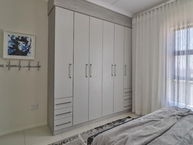 A well-maintained bedroom featuring floor-to-ceiling built-in cupboards with a modern light wood finish and neutral tiled flooring.
