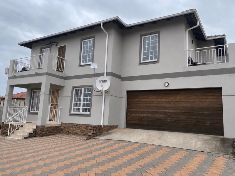 Two-story residential property featuring a double garage, paved driveway, and upper-level balcony with neutral exterior paint finish.