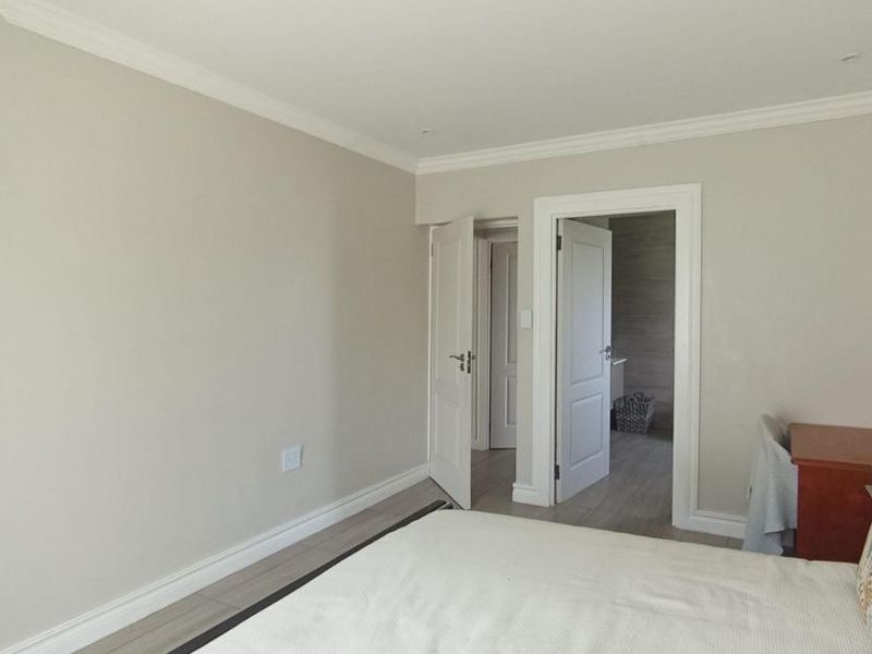 A well-maintained bedroom featuring neutral walls, built-in cupboards, coving, and tiled flooring, with direct access to an adjoining room.