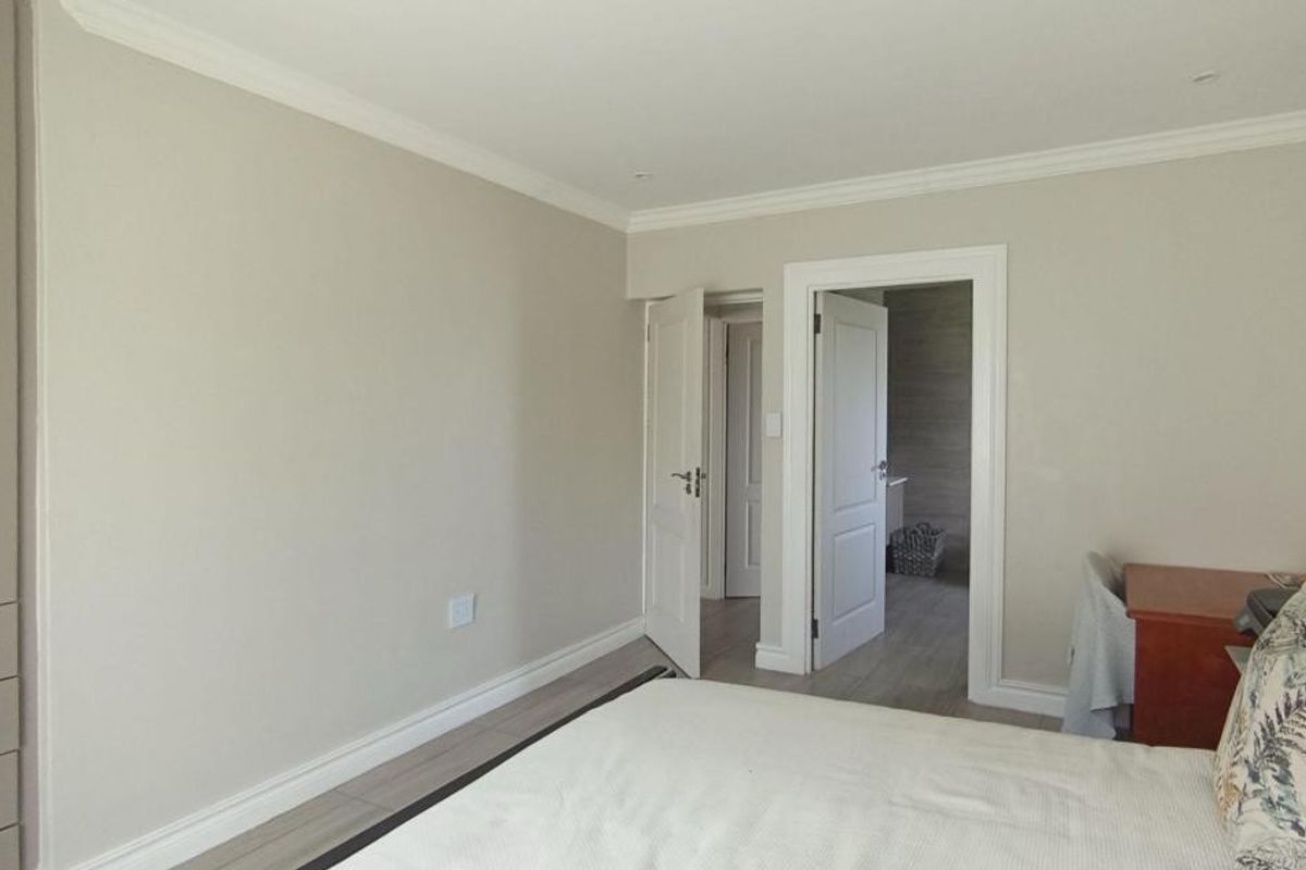 A well-maintained bedroom featuring neutral walls, built-in cupboards, coving, and tiled flooring, with direct access to an adjoining room.