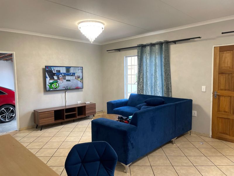 A living room featuring ceramic tile flooring, a crystal chandelier, and a wooden door, providing a functional and neutral living space.