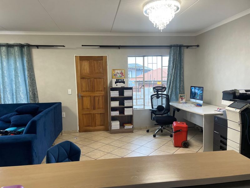 A spacious living area featuring tiled flooring, a decorative crystal chandelier, and a solid timber door, offering a functional layout for versatile use.