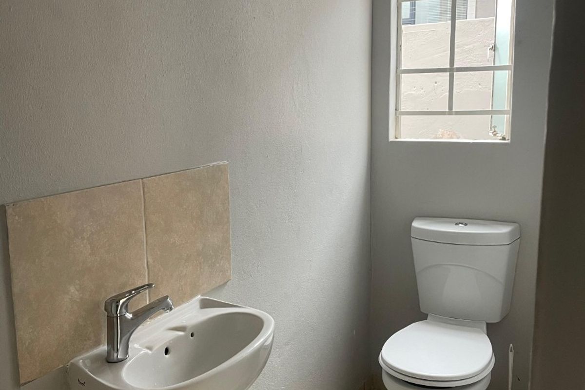 A compact guest bathroom featuring a wall-mounted basin with tiled splashback, a standard ceramic toilet, and tiled flooring.