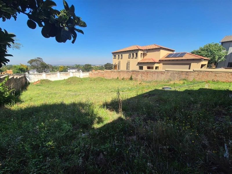 A large, undeveloped residential plot featuring perimeter brick walling and views of neighboring properties with solar installations.