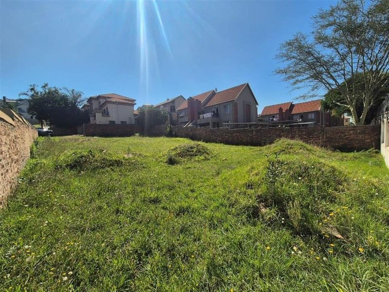 An expansive, undeveloped residential plot enclosed by brick boundary walls, featuring natural grass coverage and surrounding suburban housing.