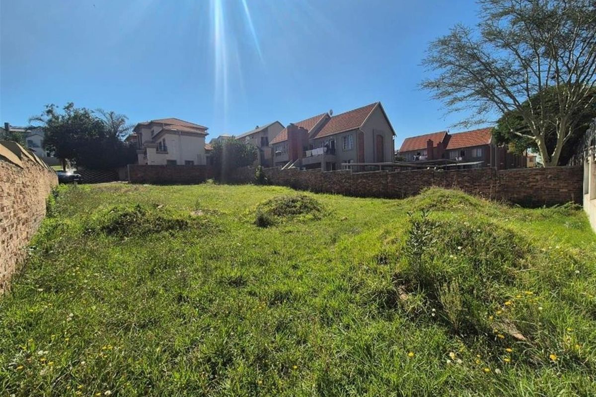 An expansive, undeveloped residential plot enclosed by brick boundary walls, featuring natural grass coverage and surrounding suburban housing.