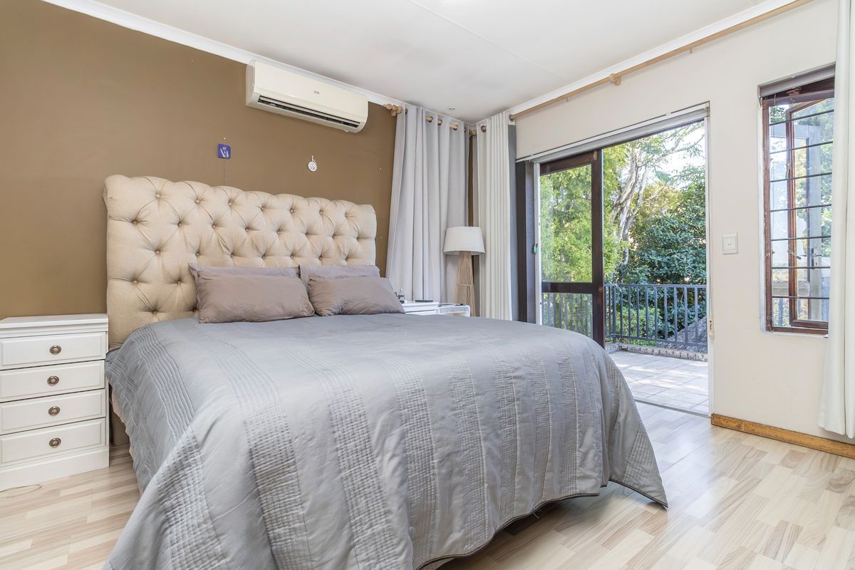 A well-lit bedroom featuring laminate flooring, a wall-mounted air conditioner, and direct access to an outdoor balcony through a sliding glass door.