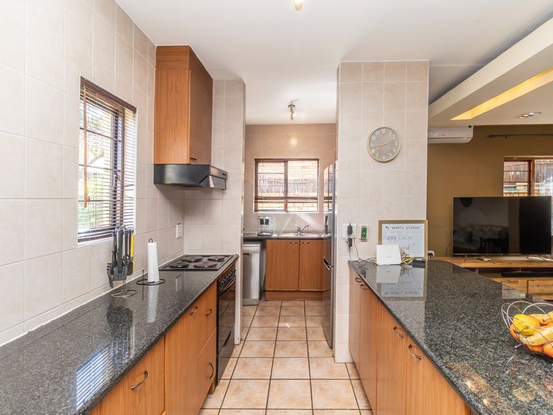 Open-plan kitchen featuring granite countertops, built-in wooden cabinetry, electric hob with extractor, and a breakfast bar, seamlessly connecting to the living area.