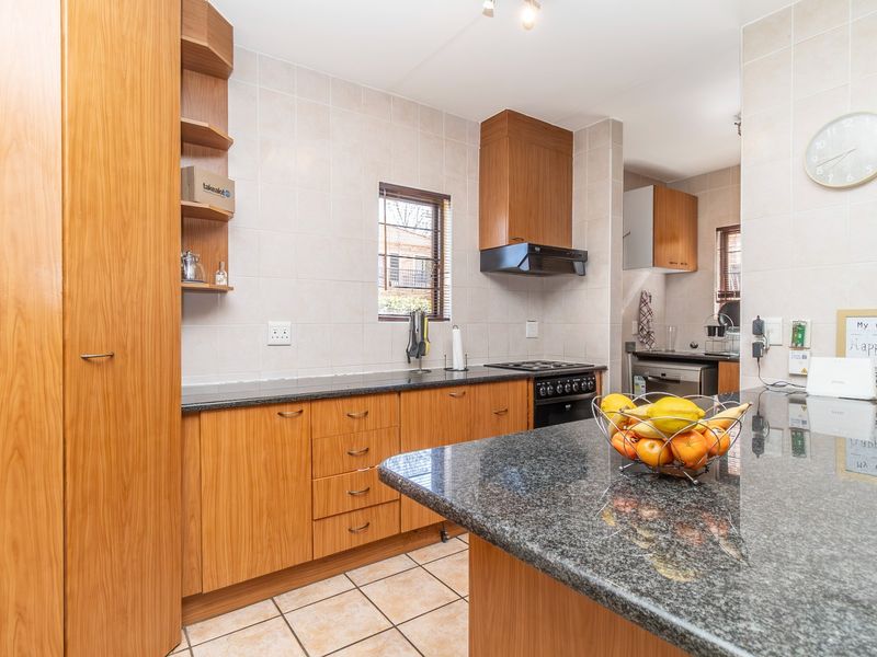 A functional kitchen featuring wooden cabinetry, granite countertops, a breakfast bar, and built-in appliances with a tiled backsplash and flooring.