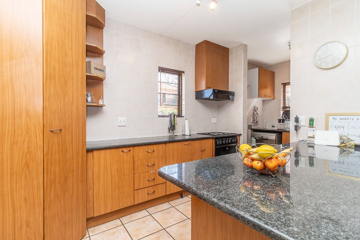 A functional kitchen featuring wooden cabinetry, granite countertops, a breakfast bar, and built-in appliances with a tiled backsplash and flooring.