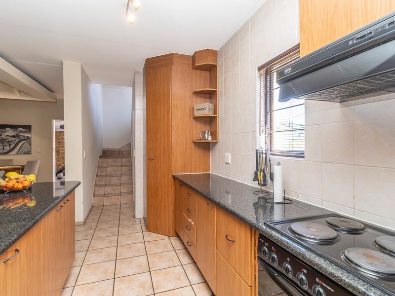 A functional kitchen featuring granite countertops, wooden cabinetry, an electric hob with extractor fan, and tiled flooring, leading to an internal staircase.