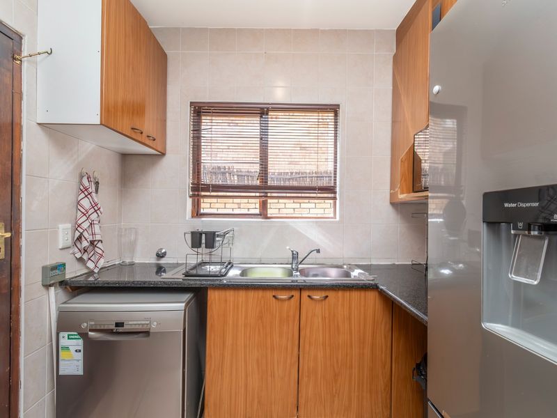 A functional kitchen featuring wood-finish cabinetry, granite countertops, a stainless steel double sink, and tiled wall finishes.