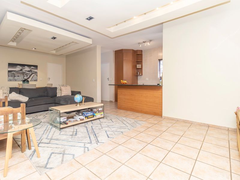 Open-plan living area featuring tiled flooring, a recessed ceiling with downlights, and a kitchen breakfast bar with built-in cabinetry.