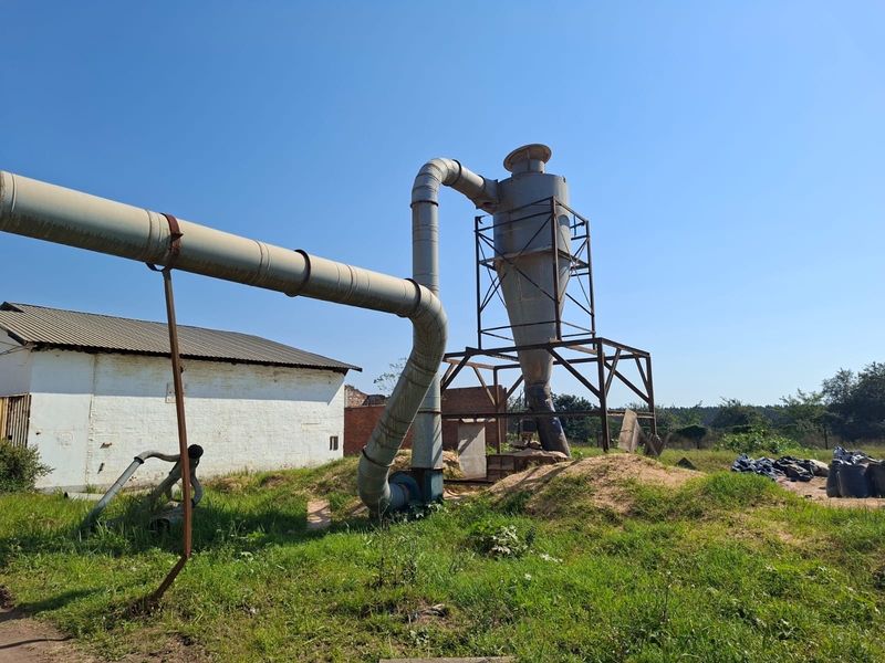 Industrial outdoor utility area featuring a large cyclone dust collection system with extensive metal ducting and steel support framework.