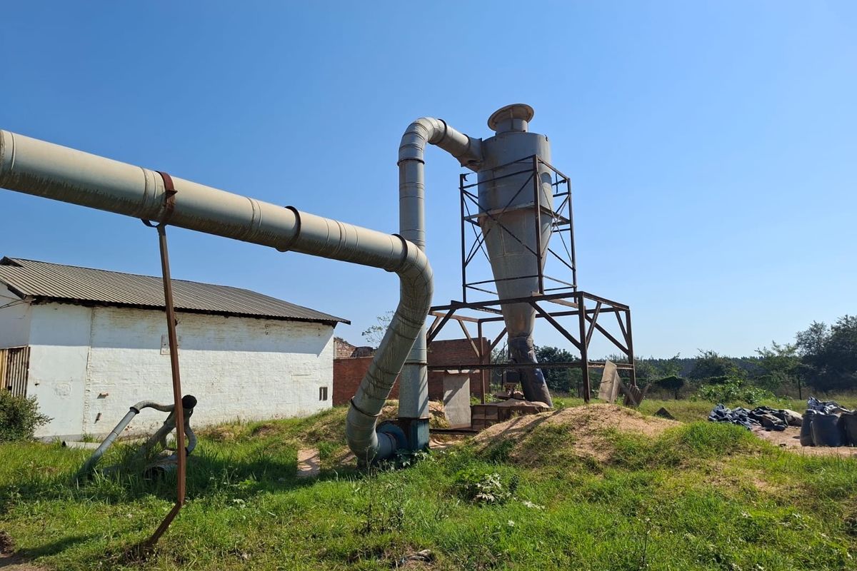 Industrial outdoor utility area featuring a large cyclone dust collection system with extensive metal ducting and steel support framework.