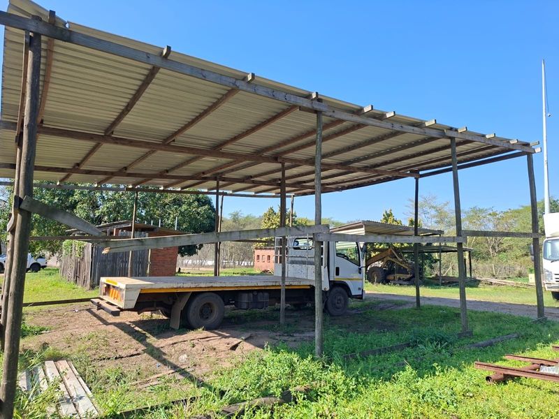 An open-sided utility shelter featuring a corrugated metal roof supported by a timber frame, suitable for vehicle or equipment storage.