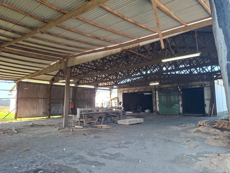 Large industrial utility space featuring high ceilings with exposed timber trusses, corrugated metal roofing, and concrete flooring, suitable for storage or workshop use.