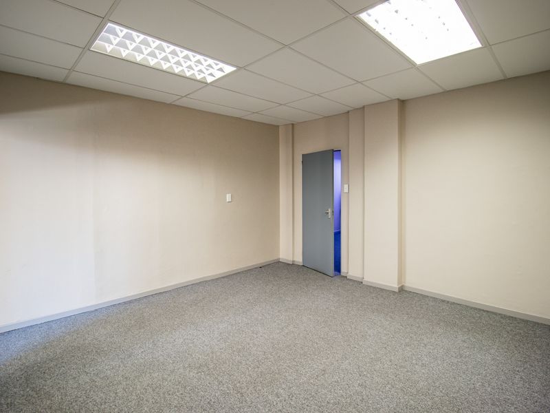 A clean, empty commercial office space featuring neutral walls, grey carpet flooring, and recessed ceiling lighting.