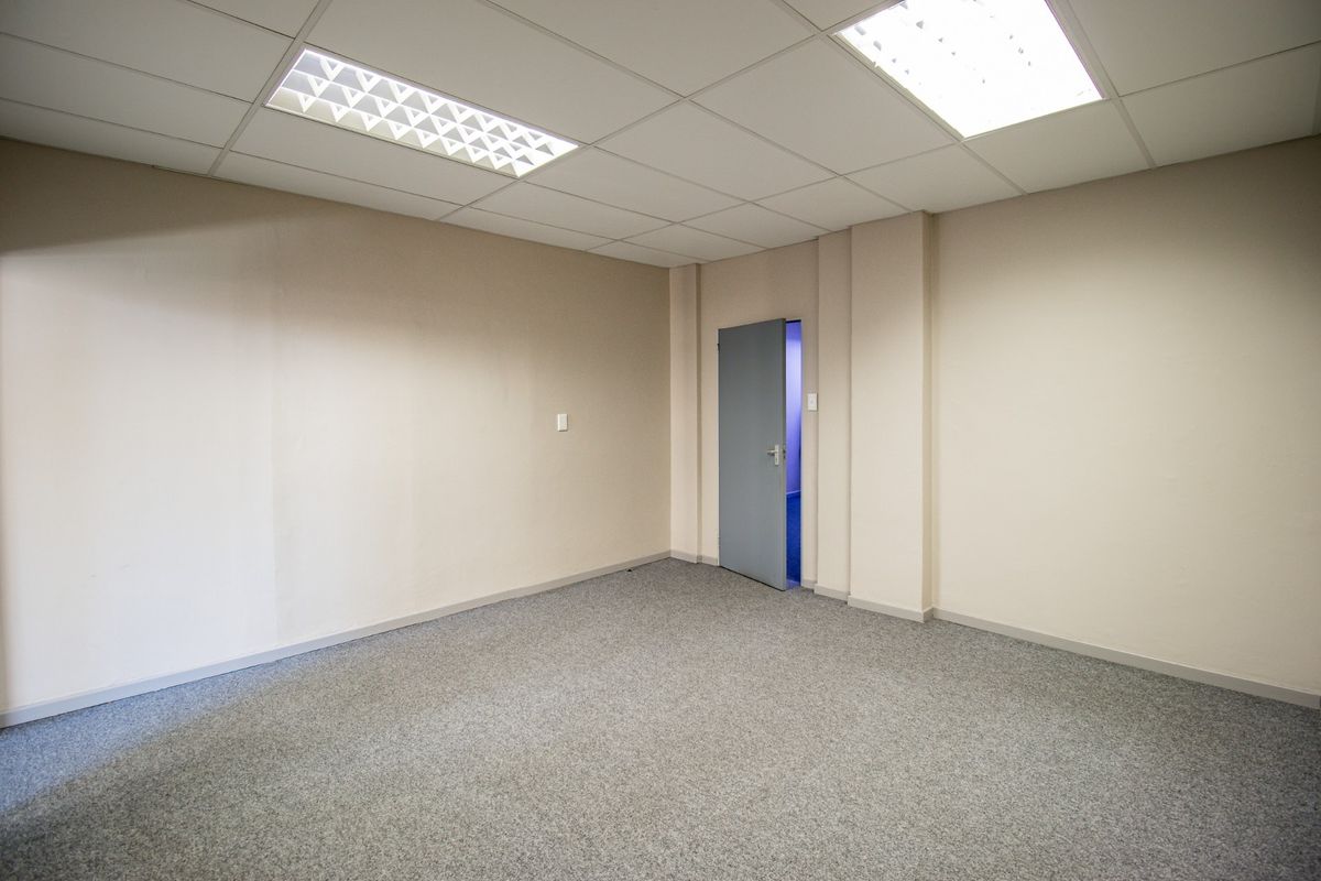 A clean, empty commercial office space featuring neutral walls, grey carpet flooring, and recessed ceiling lighting.