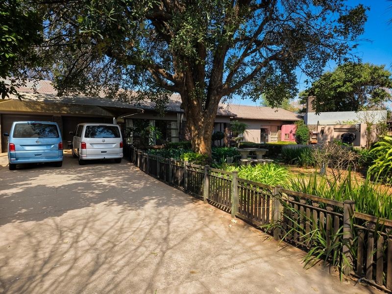 Front exterior view of the property featuring a concrete driveway, carport, mature landscaping, and a timber picket fence.