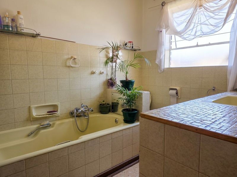 A dated bathroom featuring a built-in bathtub, tiled vanity with integrated sink, and neutral ceramic wall tiling.