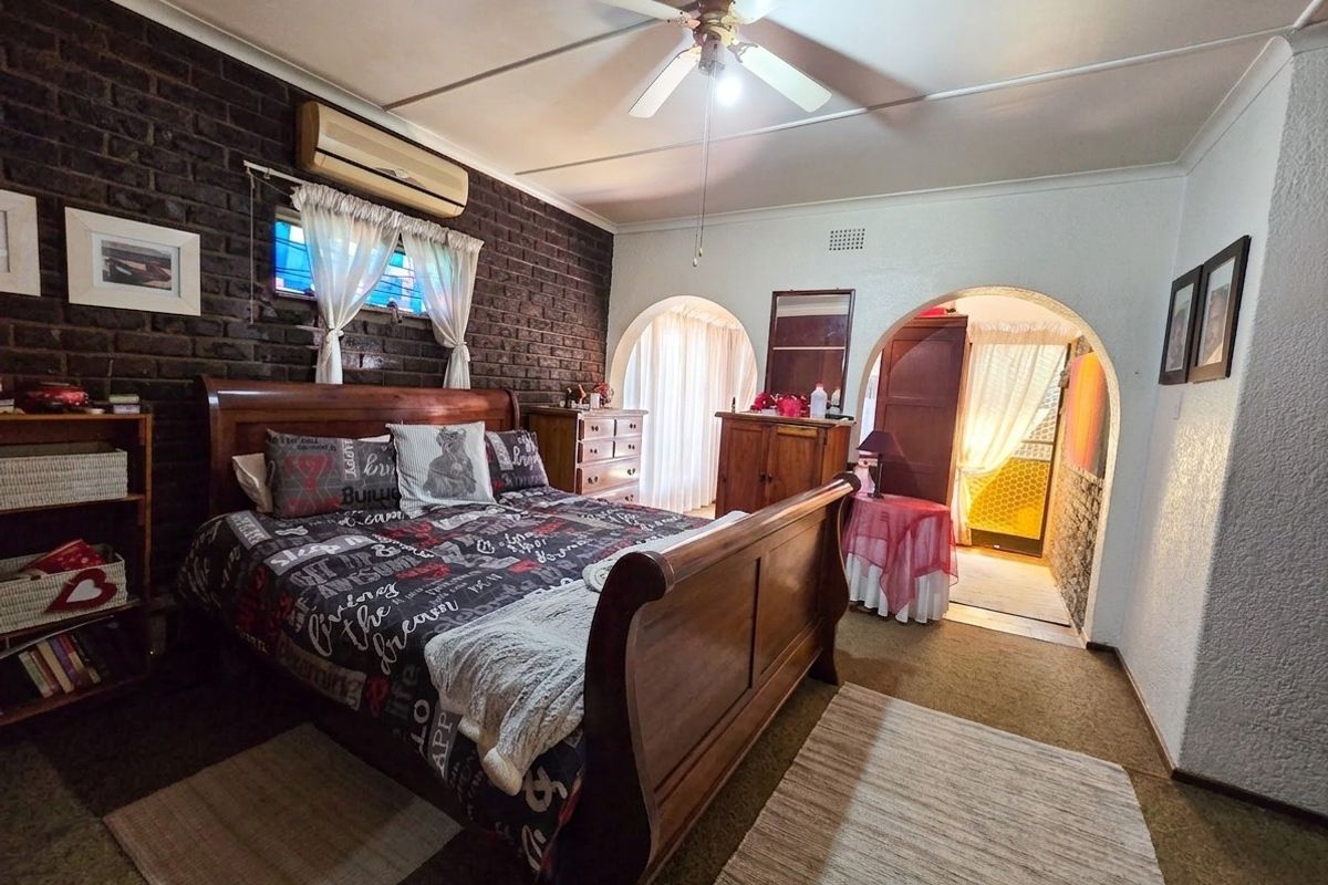 Spacious bedroom featuring an exposed brick feature wall, ceiling fan, split-system air conditioning, and distinctive arched doorways leading to adjacent areas.