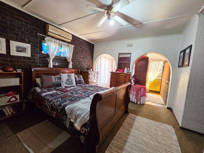 Spacious bedroom featuring an exposed brick feature wall, ceiling fan, split-system air conditioning, and distinctive arched doorways leading to adjacent areas.