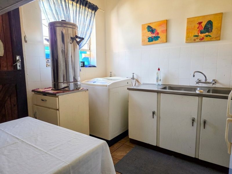 Functional laundry room featuring built-in cabinetry, a stainless steel sink, and tiled splashbacks, providing a practical space for household utility tasks.