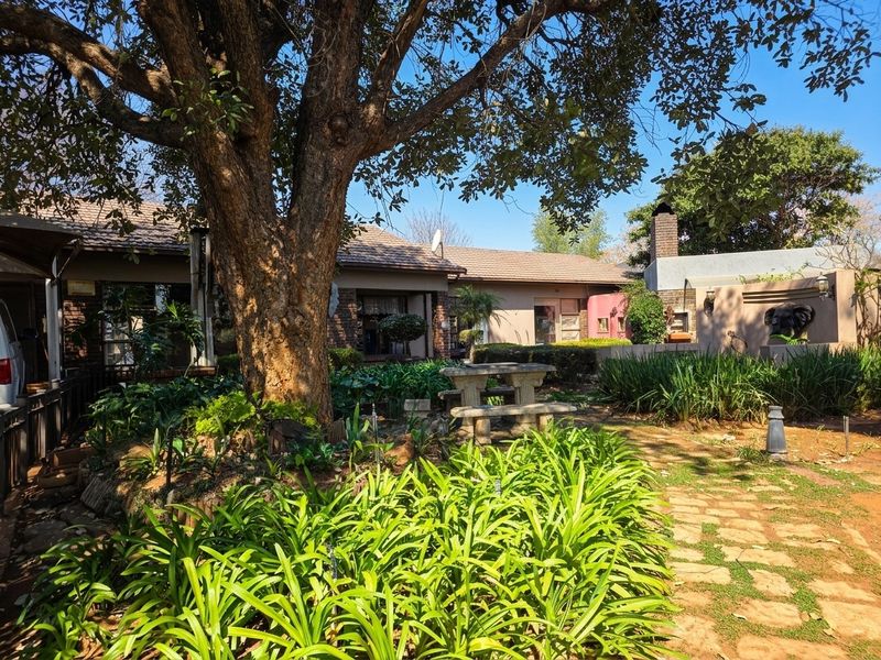A view of the rear garden featuring a mature tree, stone pathway, and a built-in outdoor fireplace against the brick facade of the house.