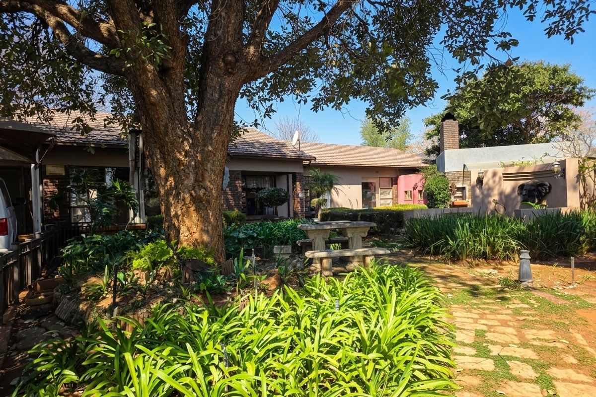 A view of the rear garden featuring a mature tree, stone pathway, and a built-in outdoor fireplace against the brick facade of the house.