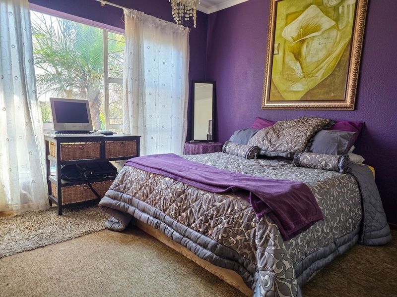 A bedroom featuring a large window allowing natural light, finished with purple wall paint and a ceiling cornice.