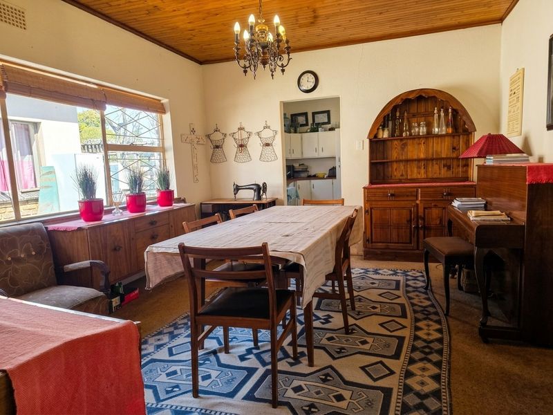 A traditional dining room featuring a warm timber ceiling, large window for natural light, and direct access to a secondary scullery or prep area.
