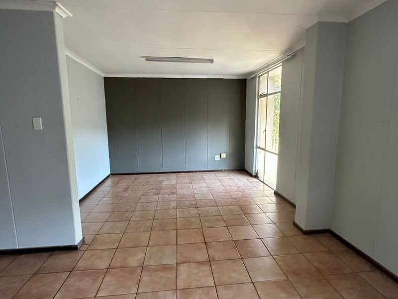 An empty, open-plan living area featuring ceramic tile flooring, neutral wall finishes, and a large glass door providing natural light.