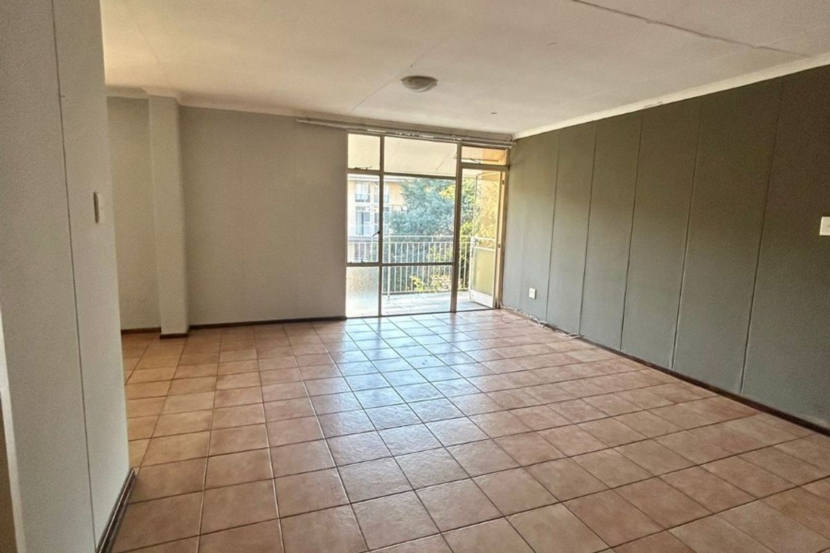 An empty, open-plan living area featuring tiled flooring, a large sliding glass door leading to a balcony, and a built-in storage cupboard.