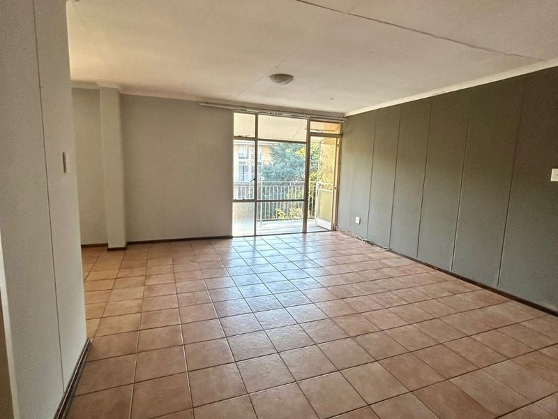 An empty, open-plan living area featuring tiled flooring, a large sliding glass door leading to a balcony, and a built-in storage cupboard.