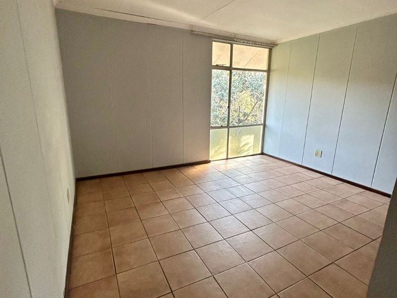 An empty bedroom featuring tiled flooring, a large window providing natural light, and neutral wall paneling, ready for renovation or staging.