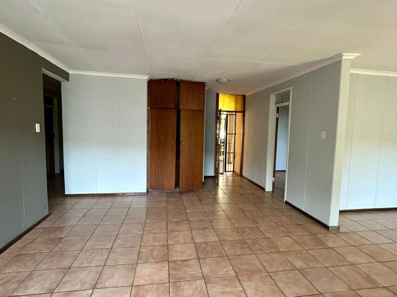 An empty, open-plan living area featuring tiled flooring, a built-in storage cupboard, and neutral wall finishes, offering a blank canvas for renovation.