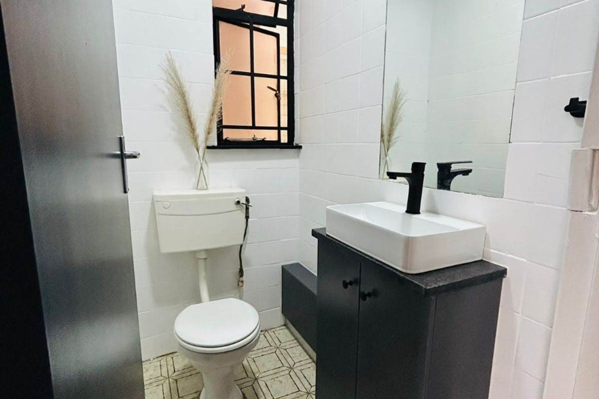 A compact bathroom featuring a modern vanity with a vessel sink, black fixtures, white wall tiling, and a window with a black frame.
