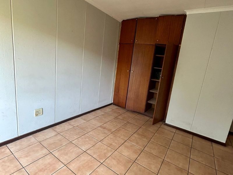 An empty bedroom featuring tiled flooring and built-in wooden cupboards, offering a blank canvas for renovation or restyling.