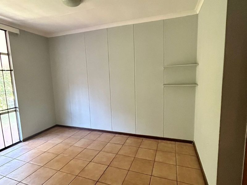 An empty bedroom featuring tiled flooring, built-in cupboards, and a sliding glass door providing natural light.