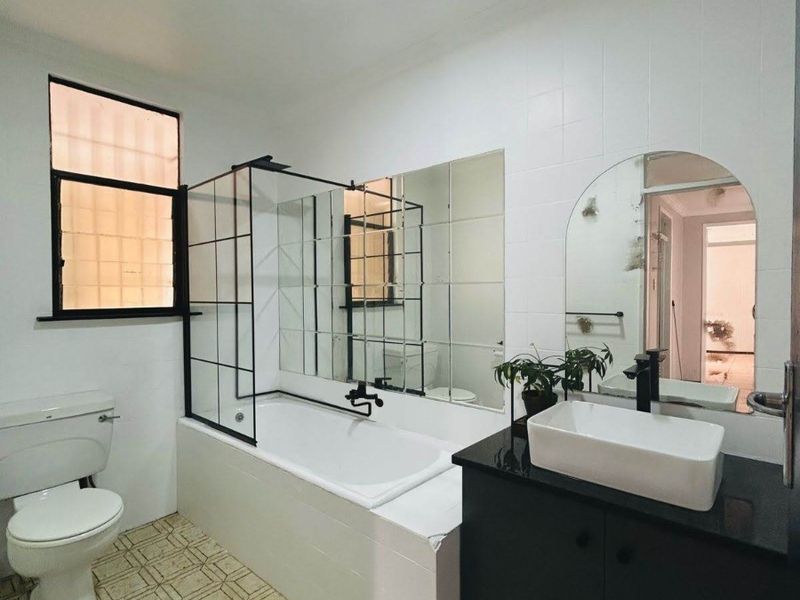 A modern-style bathroom featuring a bathtub with a black-framed screen, a vessel sink vanity, and a toilet, finished with patterned floor tiles.